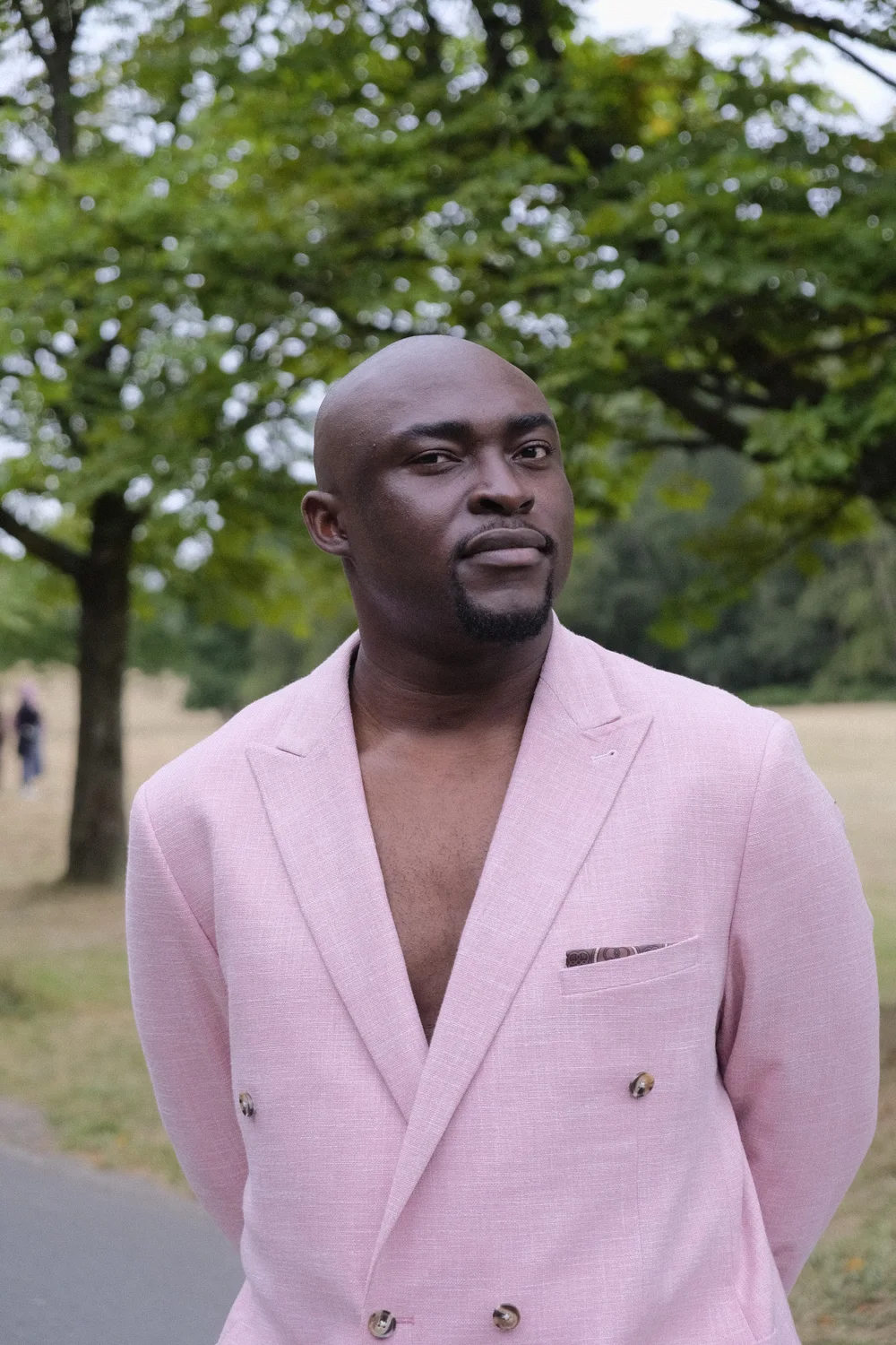 Charles Njoku in a pink blazer, standing among trees